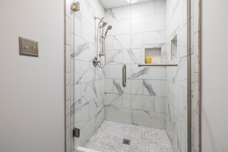 Tiled shower alcove with a glass door, wall niche and hand shower